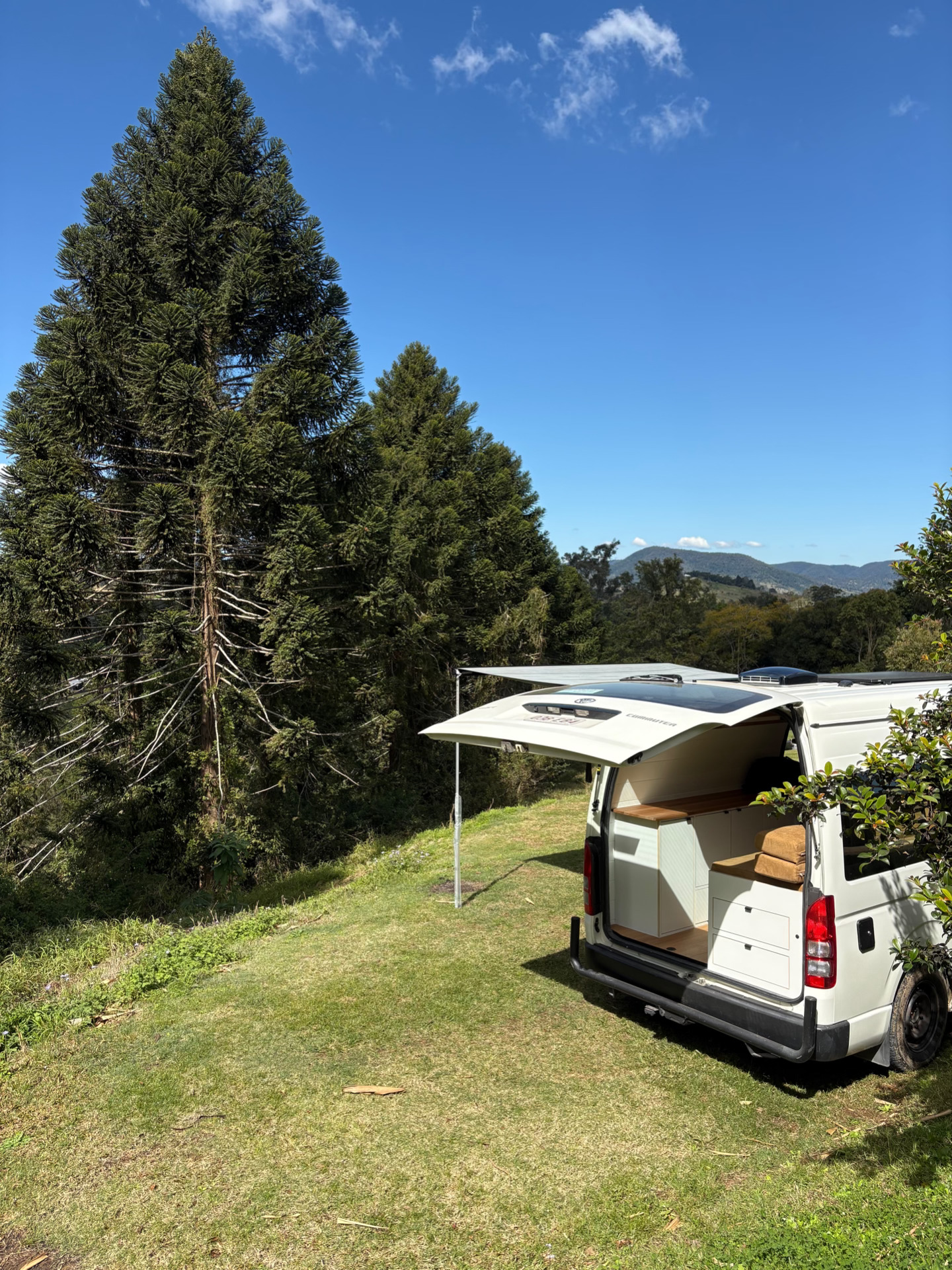 Toyota Hiace Commuter with awning out beside pine trees